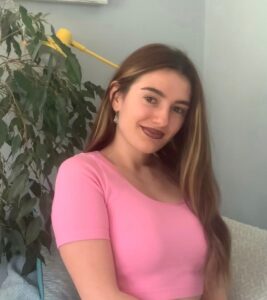 Cristina smiling in a pink top in front of a green plant